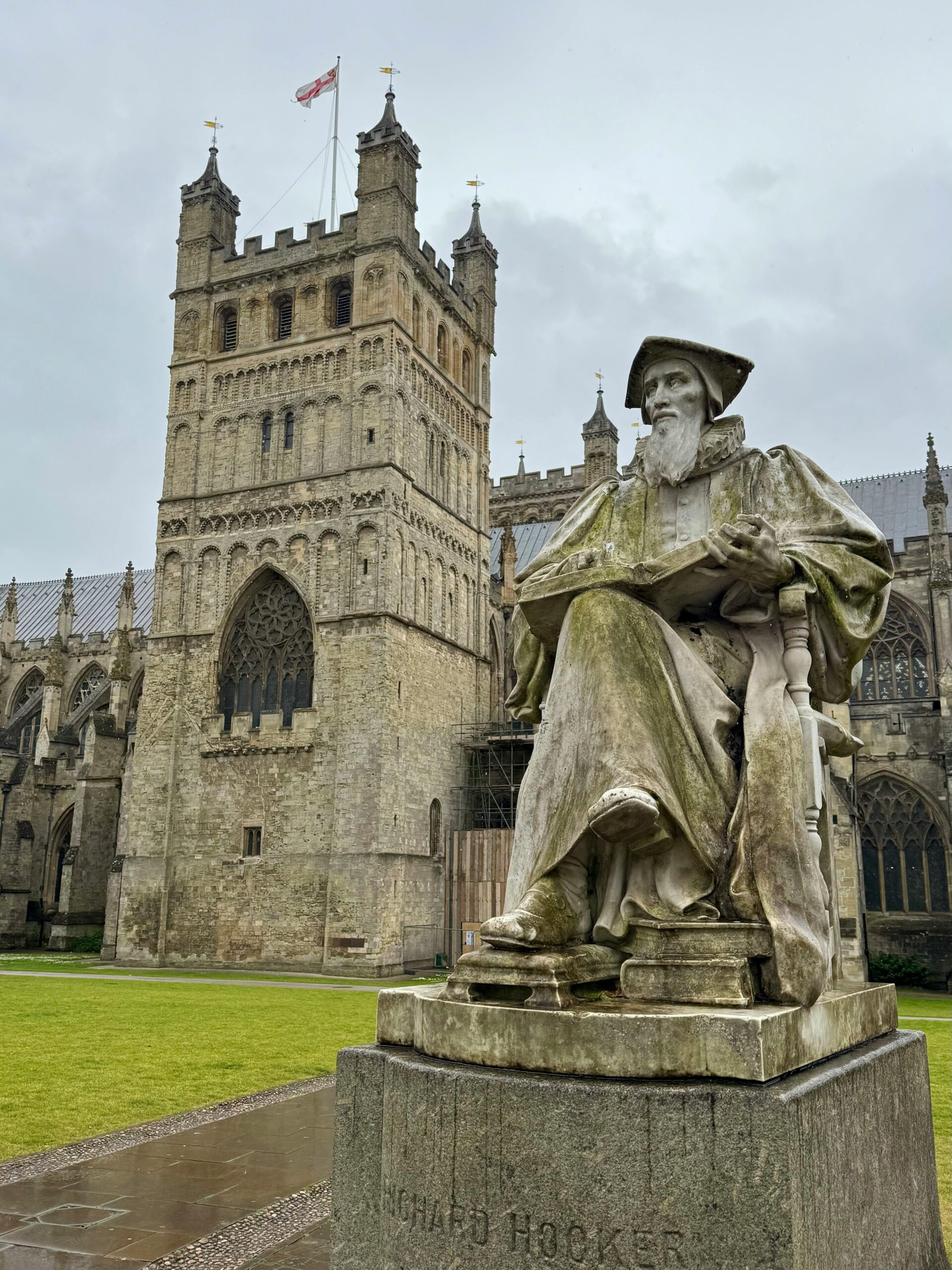 Statue of Richard Hooker in front of historic Exeter Cathedral on a cloudy day.